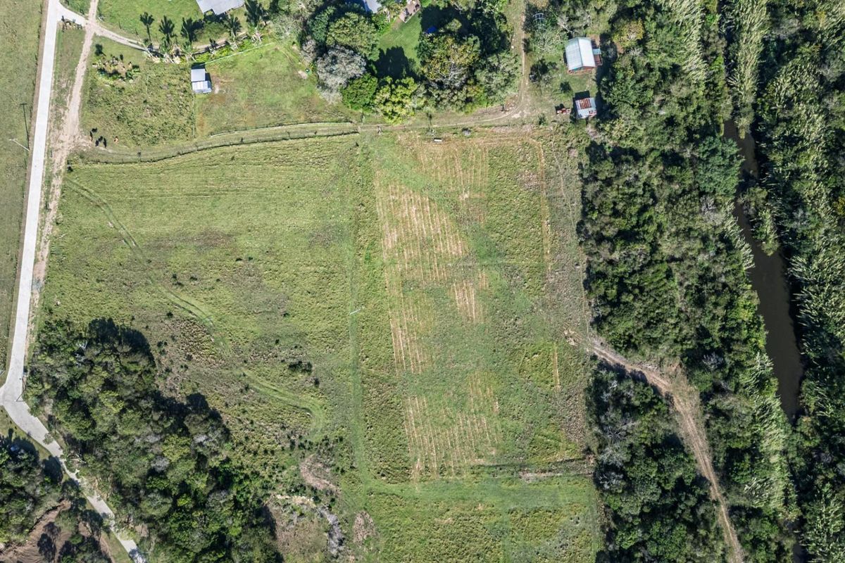 Aerial view of a vacant residential land plot featuring natural vegetation, perimeter fencing, and adjacent access road.