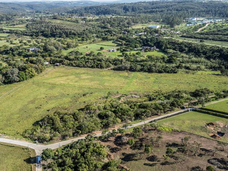 An aerial view of a large, expansive vacant residential plot featuring natural vegetation, surrounding rural landscape, and access road infrastructure.