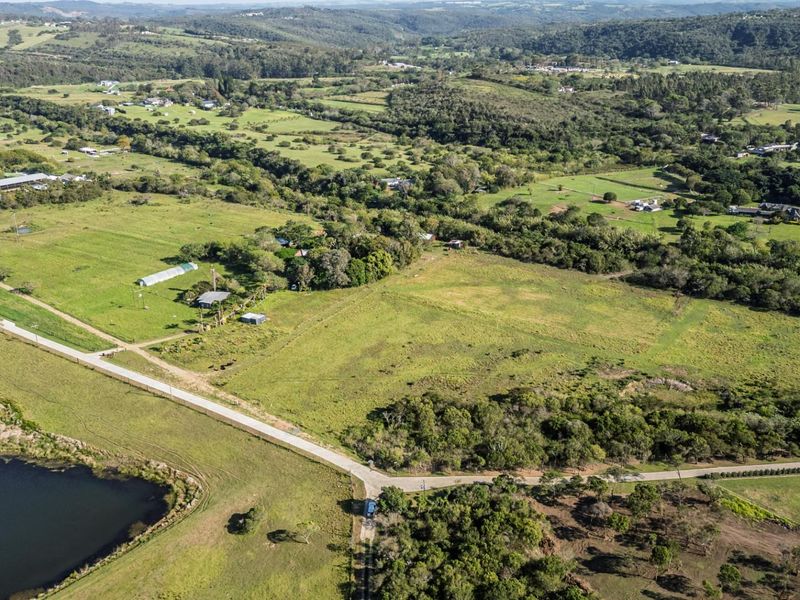 An aerial view of a large, undeveloped residential land parcel featuring open green space, access roads, and proximity to a natural water body.