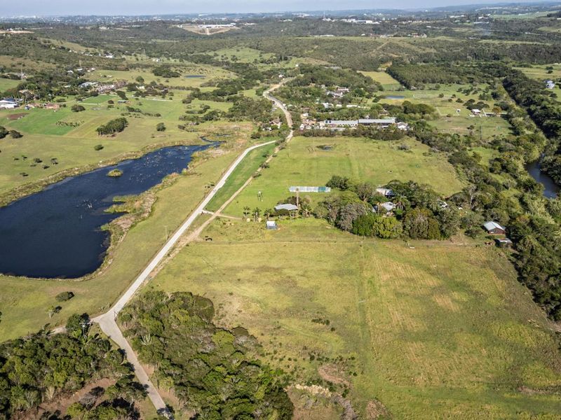 An aerial view of a large, undeveloped residential land parcel featuring natural landscape, a nearby water body, and existing access road infrastructure.