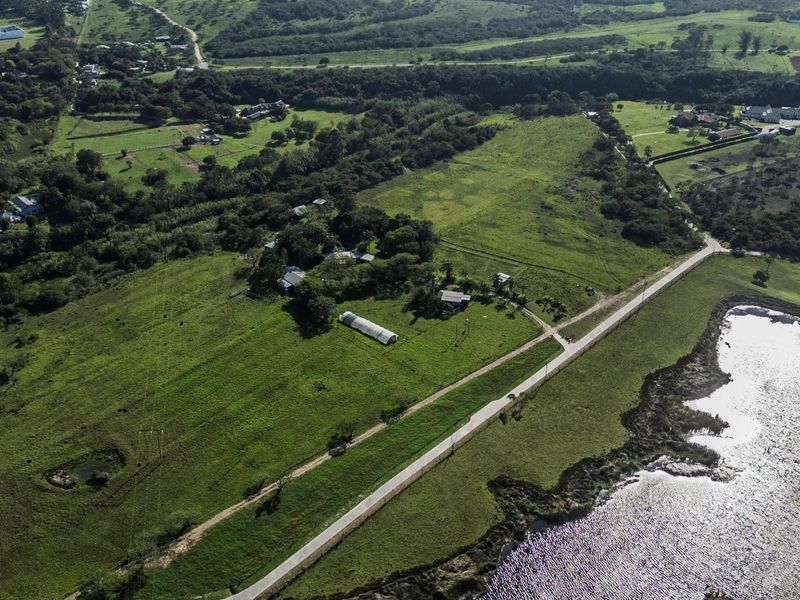 Aerial view of a large residential vacant land plot featuring open green fields, an access road, and a small water body.
