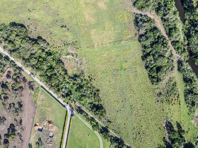 Aerial view of a large residential vacant land parcel featuring natural vegetation, access road, and scenic river frontage.