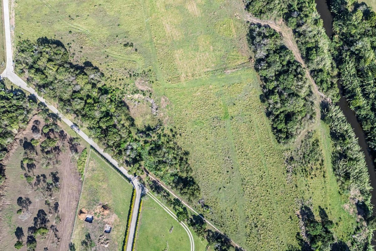 Aerial view of a large residential vacant land parcel featuring natural vegetation, access road, and scenic river frontage.
