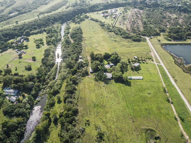 An aerial view of a large residential vacant land plot featuring natural river frontage, established vegetation, and access to local road infrastructure.