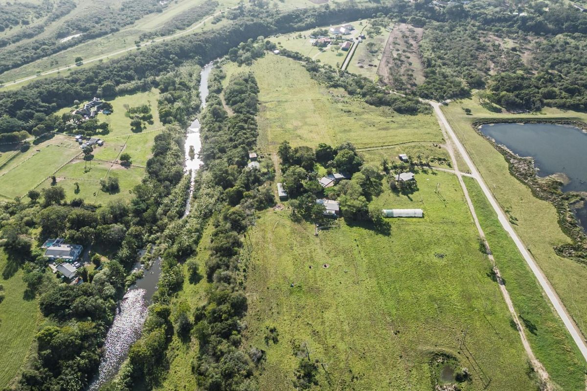 An aerial view of a large residential vacant land plot featuring natural river frontage, established vegetation, and access to local road infrastructure.
