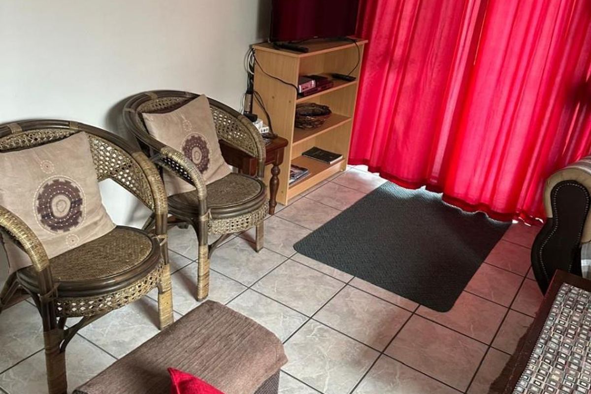 A living room area featuring tiled flooring and large windows covered by curtains, providing a functional space for relaxation.