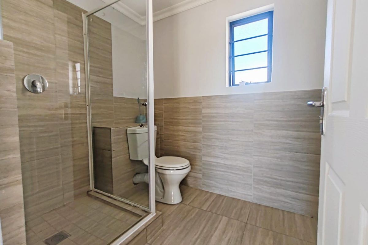 A modern bathroom featuring a glass-enclosed walk-in shower, tiled walls and flooring, and a standard toilet.