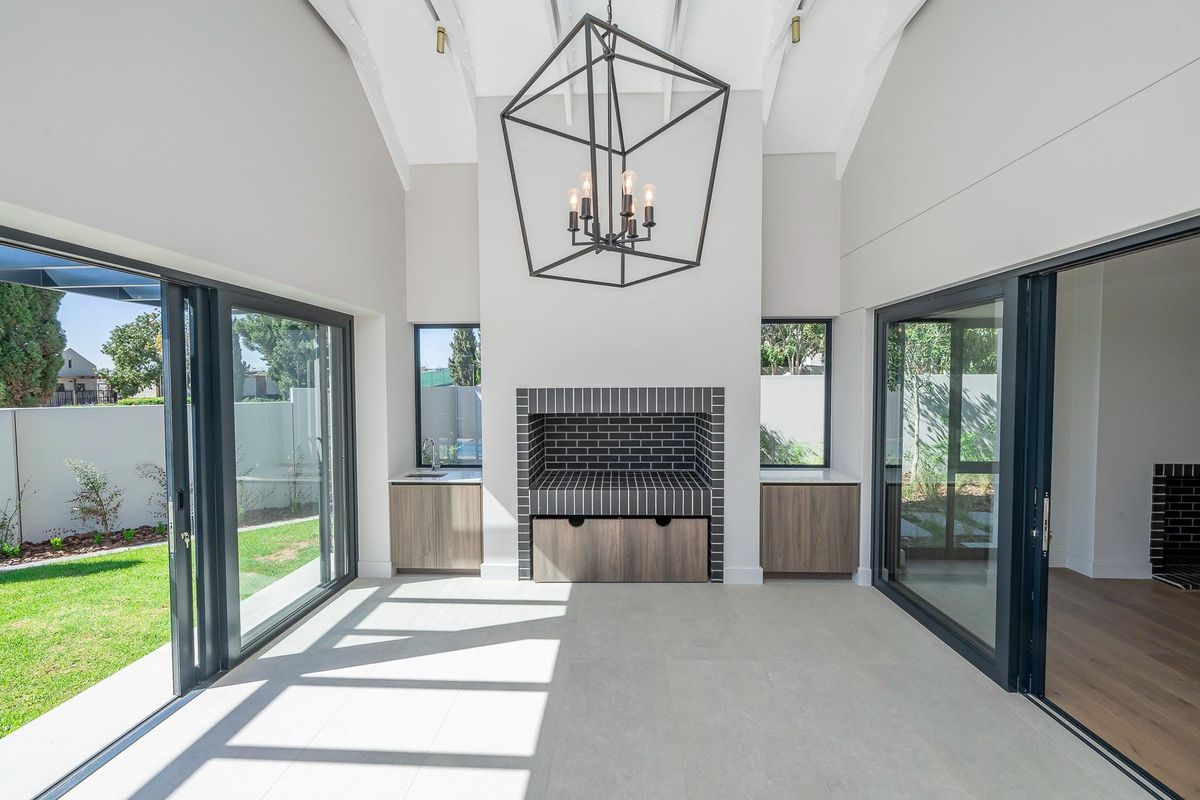 A bright, modern living space featuring a vaulted ceiling, built-in fireplace with dark brick surround, cabinetry, and large sliding glass doors opening to the garden.