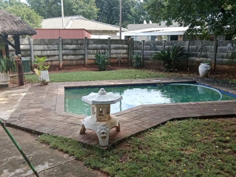 Outdoor pool area featuring a swimming pool, brick paving, and a thatched lapa structure, enclosed by a precast concrete boundary wall.