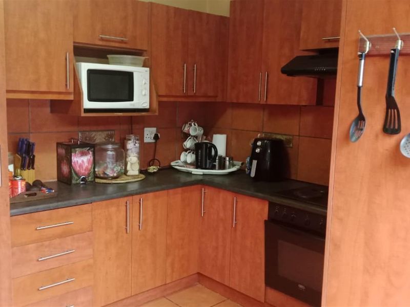 A compact kitchen featuring wood-look laminate cabinetry, dark countertops, a built-in oven with hob, and a tiled backsplash.