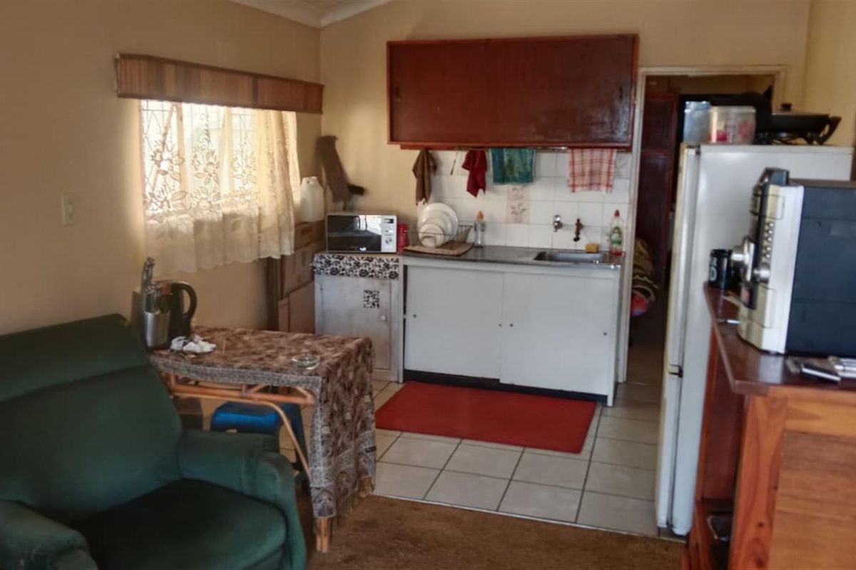 A compact kitchen area featuring basic cabinetry, a stainless steel sink, and tiled flooring, currently showing signs of age and wear.