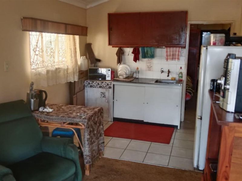 A compact kitchen area featuring basic cabinetry, a stainless steel sink, and tiled flooring, currently showing signs of age and wear.