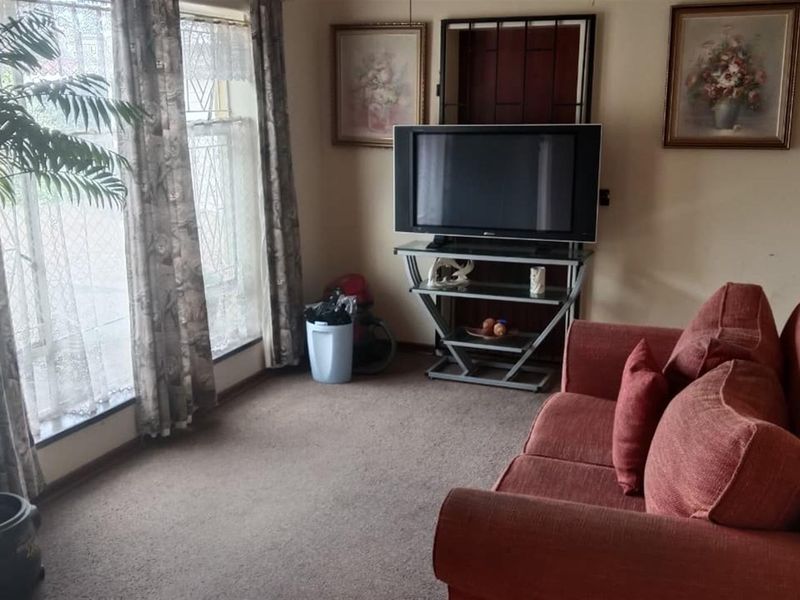 A living room featuring carpeted flooring and a security gate over the window, providing a functional and lived-in space.