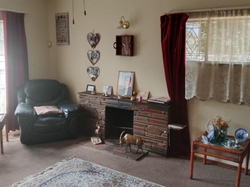 A living room featuring a traditional stone fireplace and security bars on the windows, with carpeted flooring throughout.