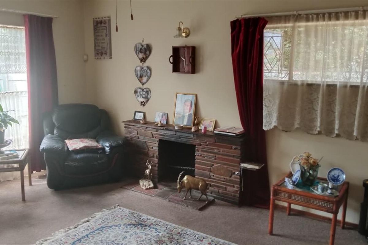 A living room featuring a traditional stone fireplace and security bars on the windows, with carpeted flooring throughout.