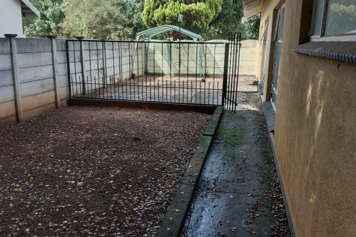 Rear exterior area featuring a concrete pathway, gravel ground cover, and secure metal fencing along the precast concrete boundary wall.
