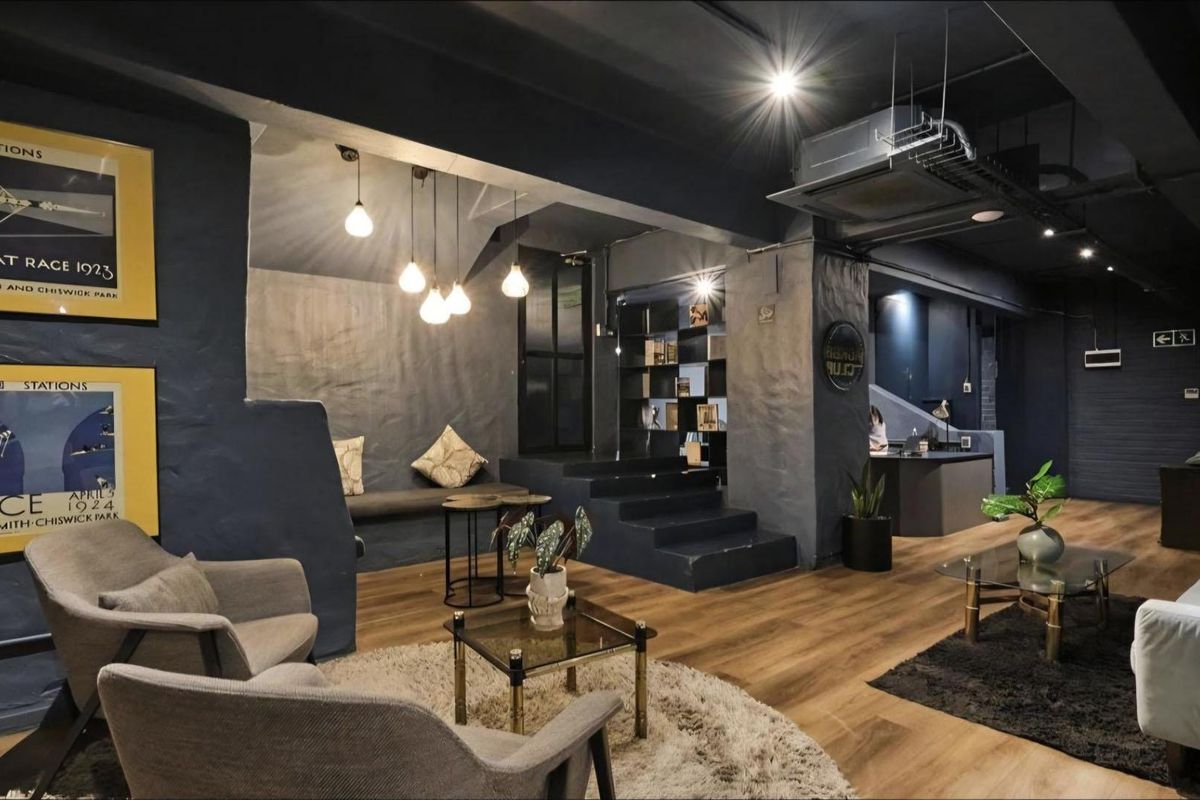 A modern, industrial-style living area featuring dark painted walls, exposed ceiling ducting, hardwood flooring, and integrated bench seating with recessed lighting.