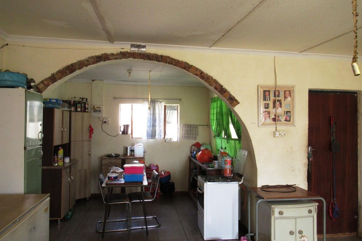 A dated kitchen area featuring a prominent brick archway, tiled flooring, and basic cabinetry, offering potential for renovation and modernization.