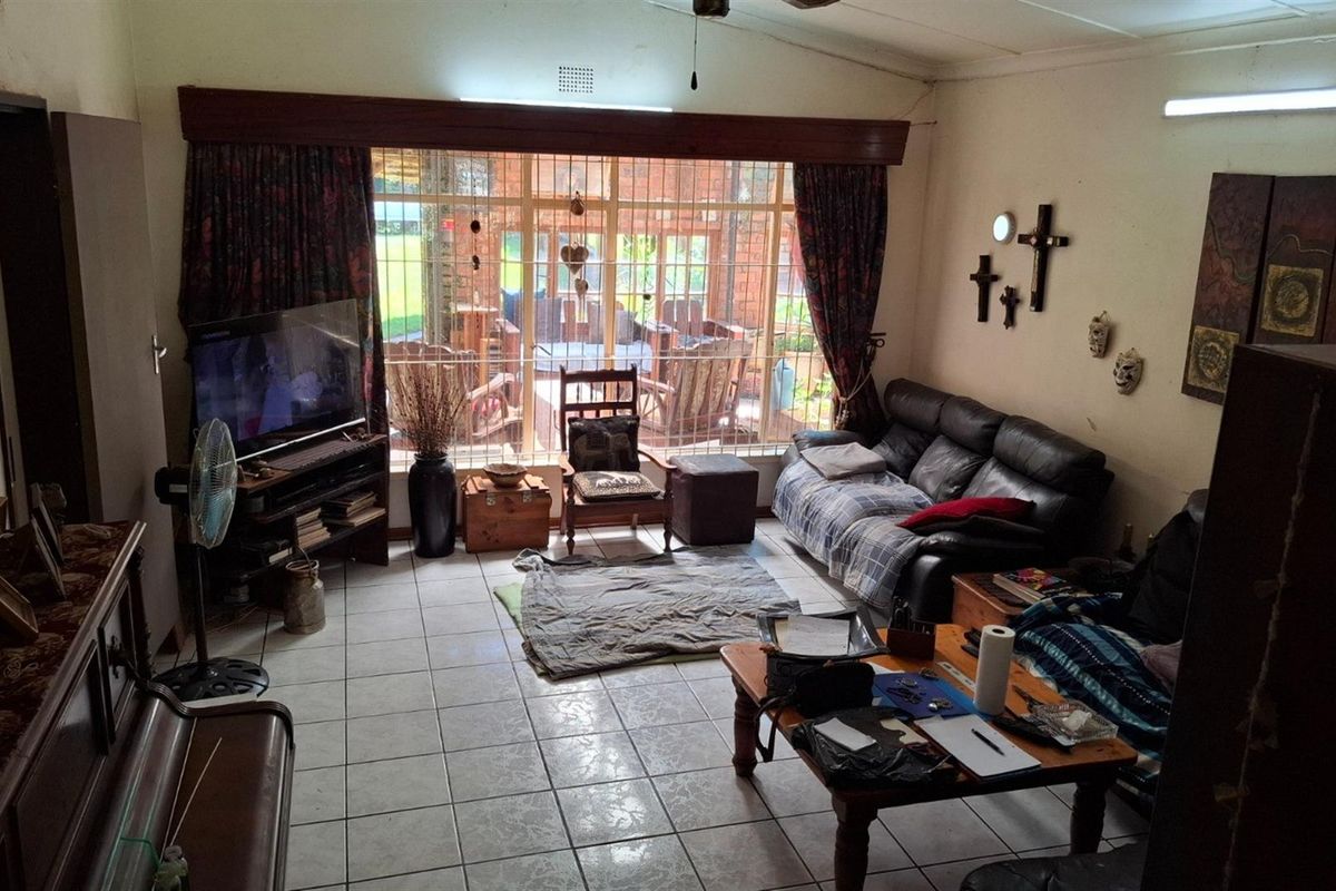 A living room featuring tiled flooring and large windows with security bars, providing natural light and a view of the outdoor patio area.