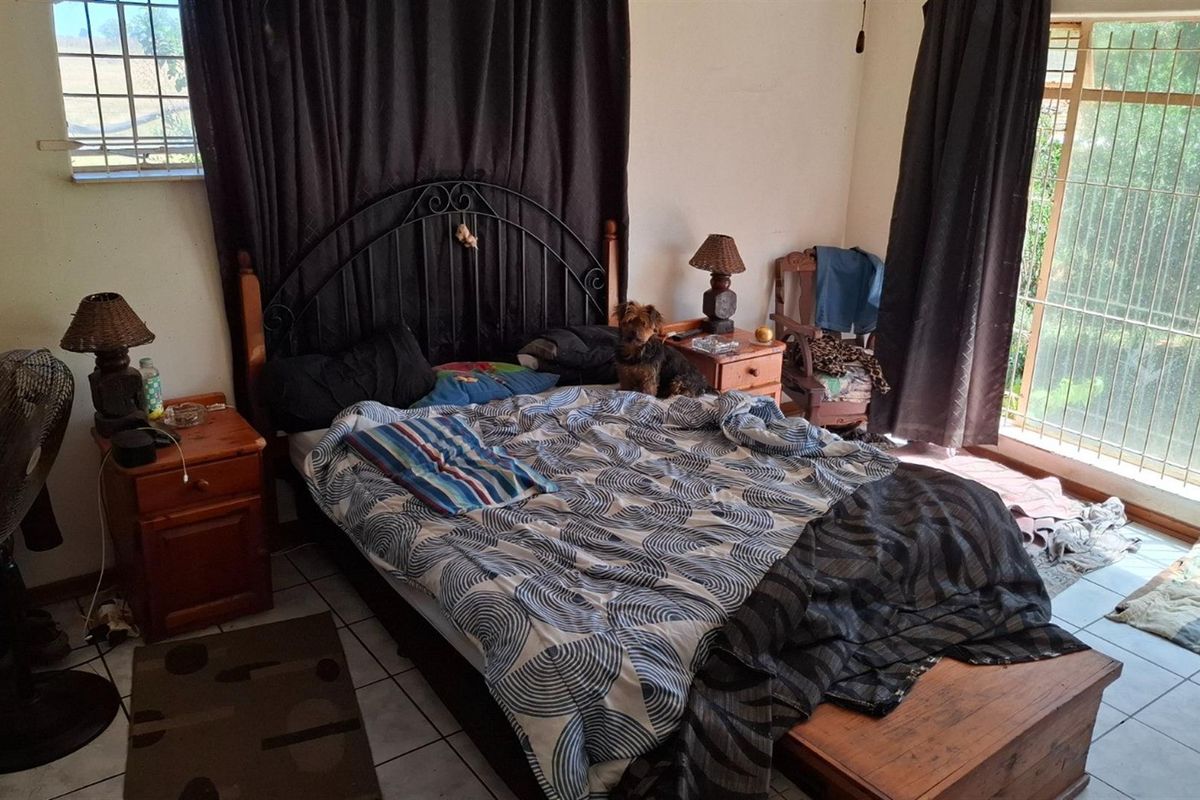 A bedroom featuring tiled flooring and large windows with security bars, providing natural light and access to the exterior.