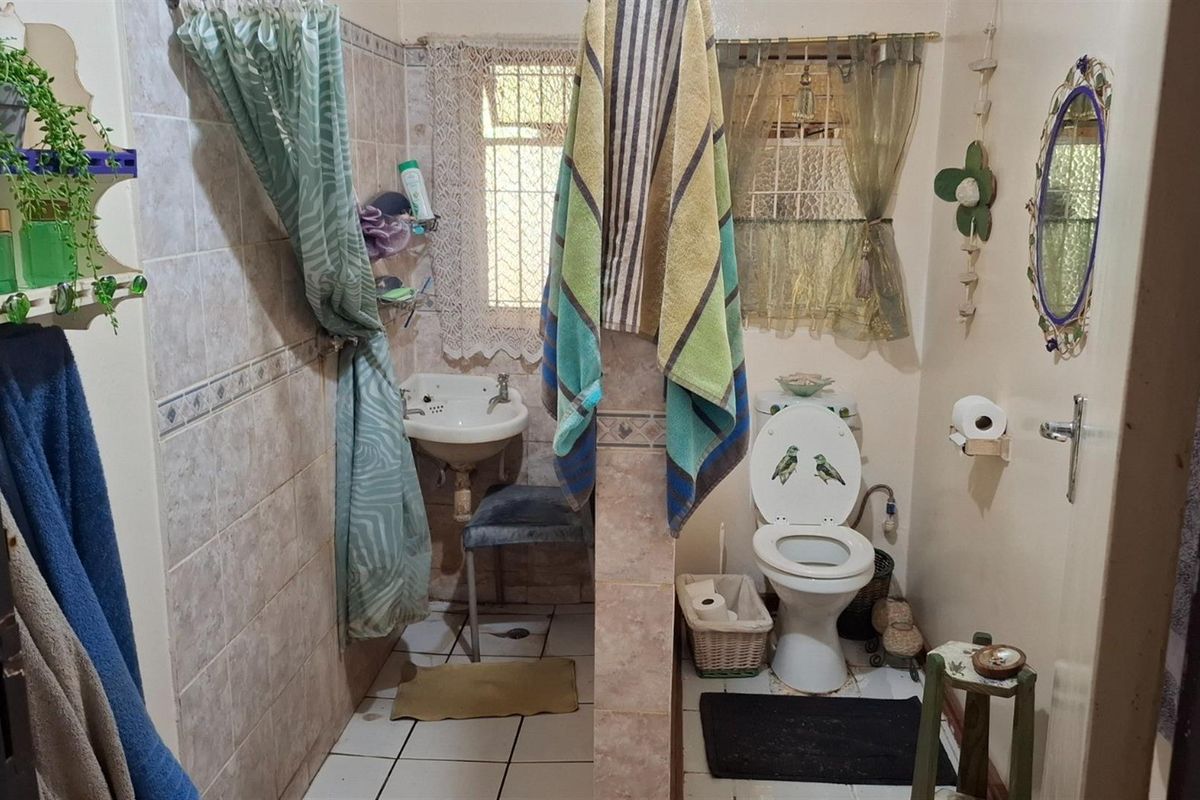 A functional bathroom featuring a shower area with tiled walls, a pedestal basin, and a standard toilet, requiring minor cosmetic updates.