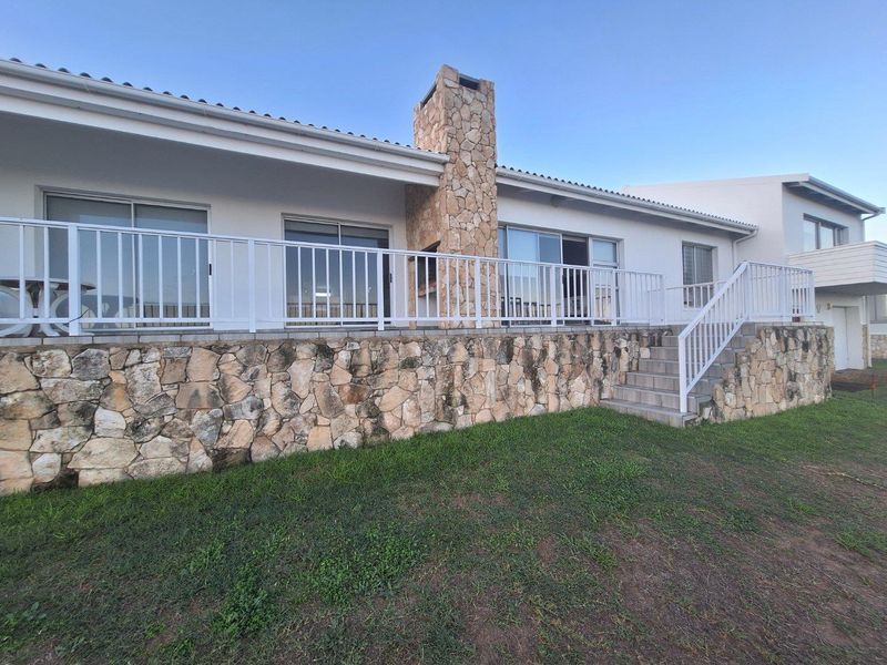 Rear exterior view featuring a raised patio with white railings, stone-clad chimney, and stairs leading down to the garden area.