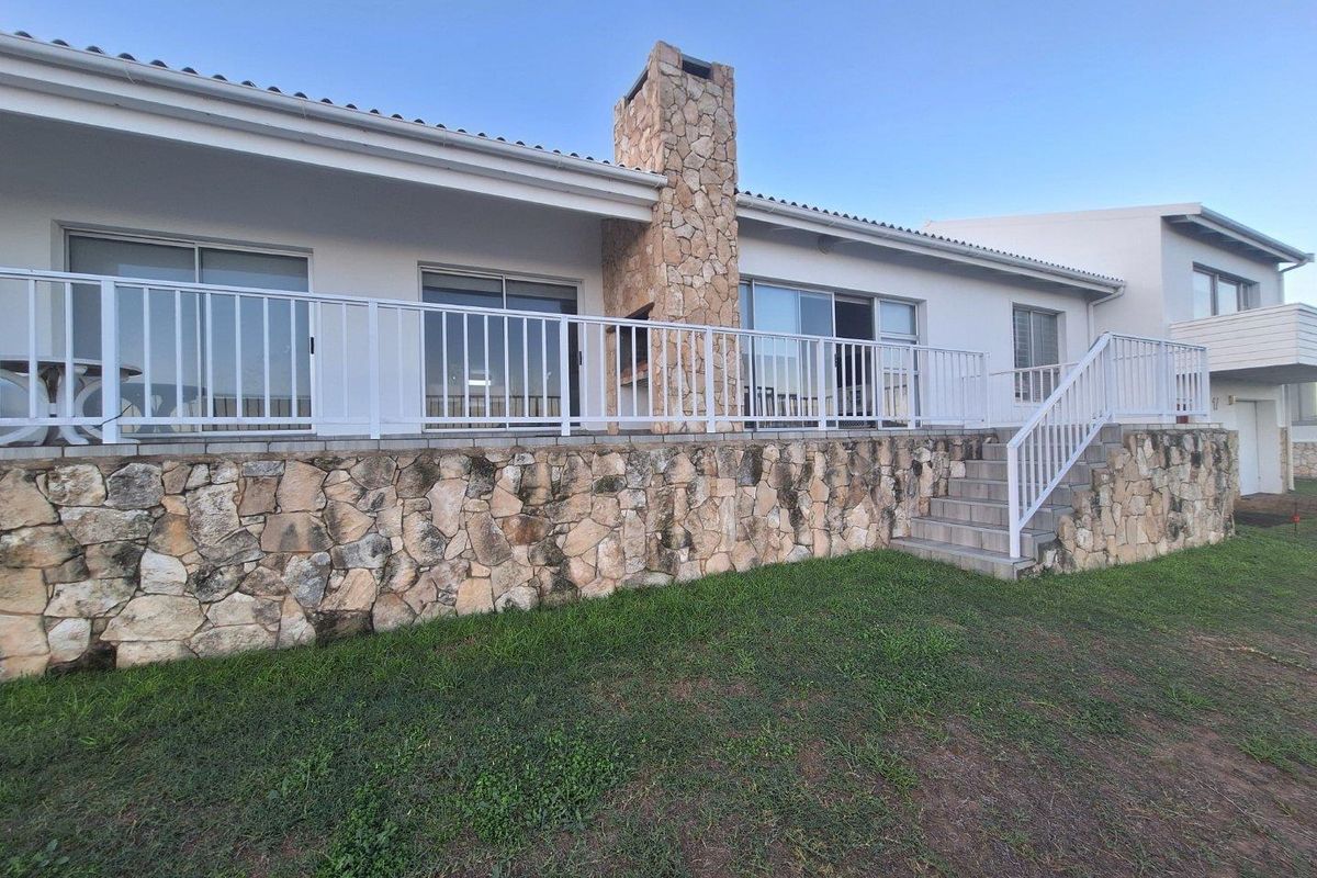 Rear exterior view featuring a raised patio with white railings, stone-clad chimney, and stairs leading down to the garden area.