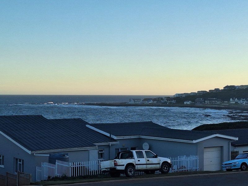 A coastal property view featuring a residential house with a metal roof, garage, and white picket fencing overlooking the ocean.