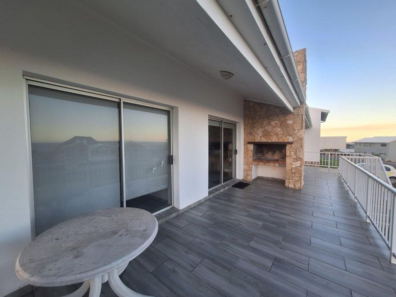 Spacious covered patio featuring modern grey floor tiles, a built-in stone fireplace, and sliding glass doors providing seamless indoor-outdoor flow.
