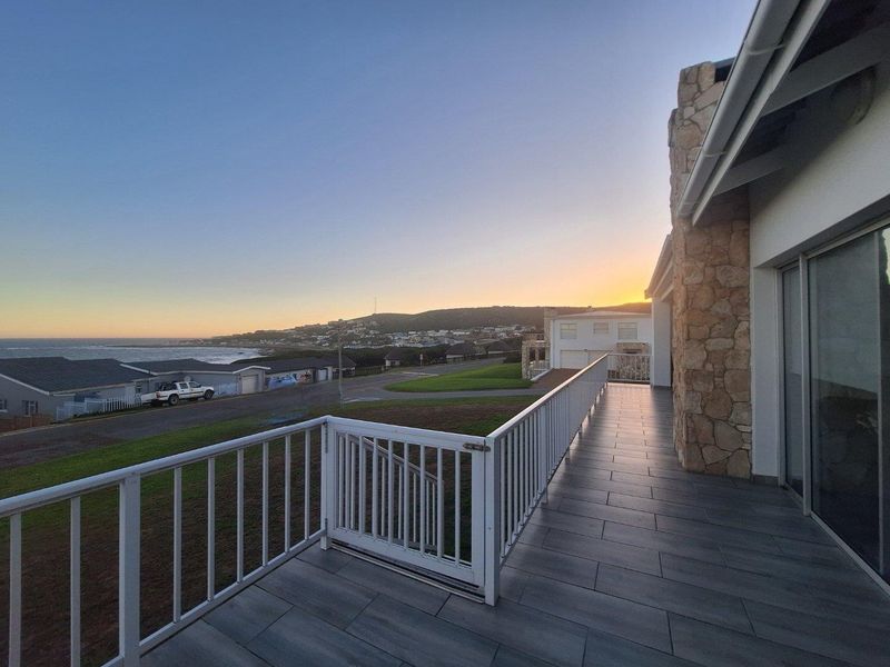 Spacious elevated balcony featuring modern tiled flooring, white metal railings, and scenic coastal views at sunset.
