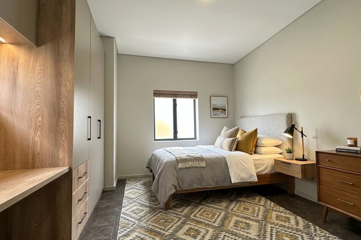 A modern, well-lit bedroom featuring built-in wooden cabinetry, integrated desk space, and neutral finishes, creating a clean and functional living environment.