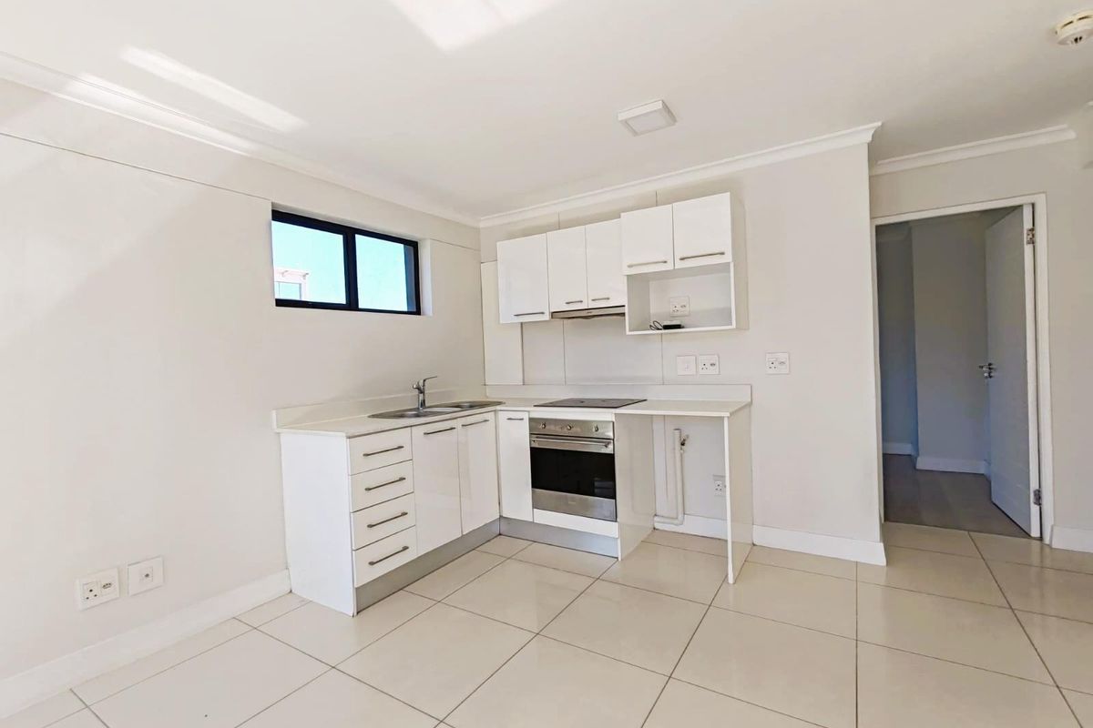 A clean, modern kitchen featuring white cabinetry, a built-in oven, hob, extractor fan, and tiled flooring in an open-plan layout.