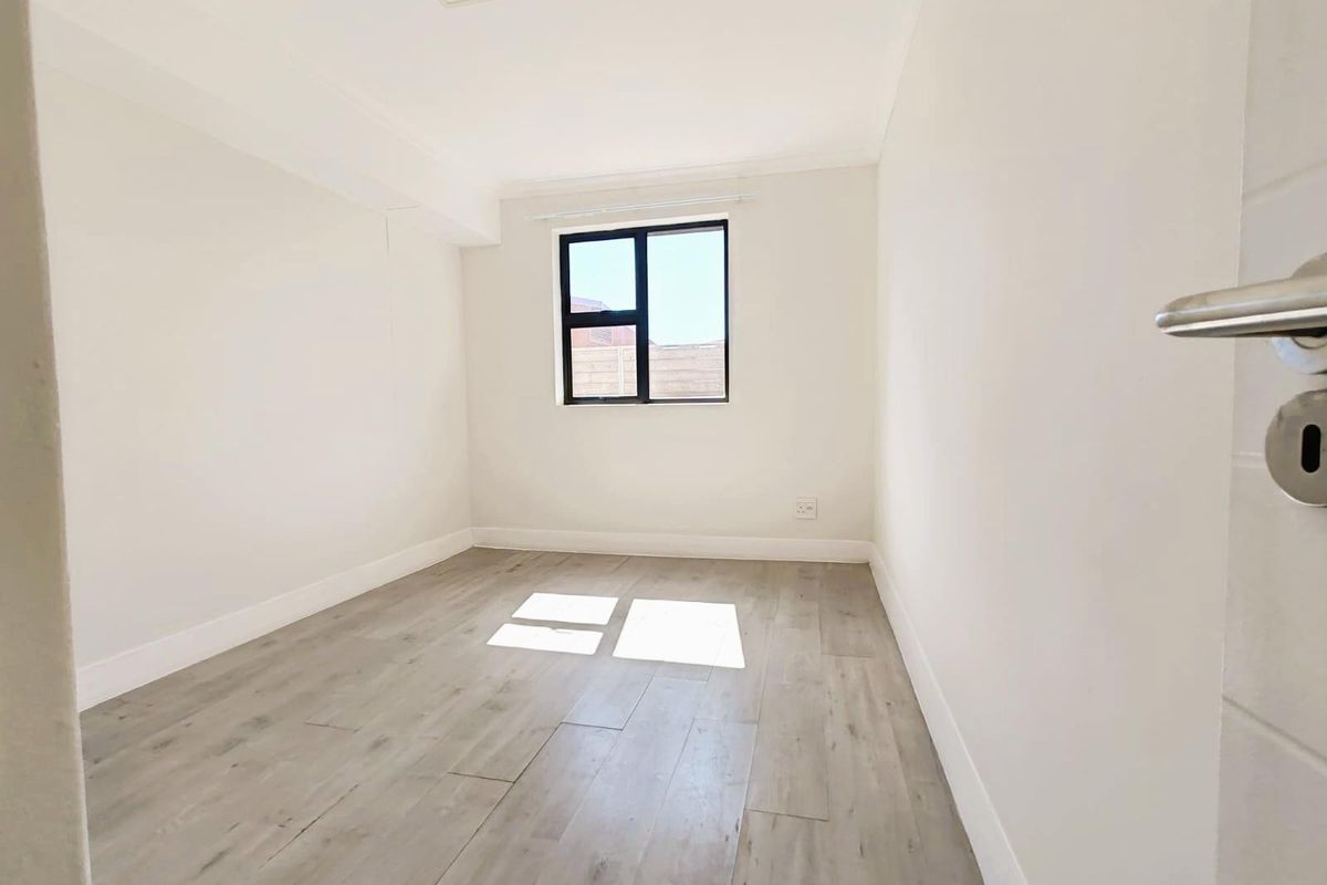 A bright, empty bedroom featuring modern light-toned wood-look flooring, neutral walls, and a window providing natural light.