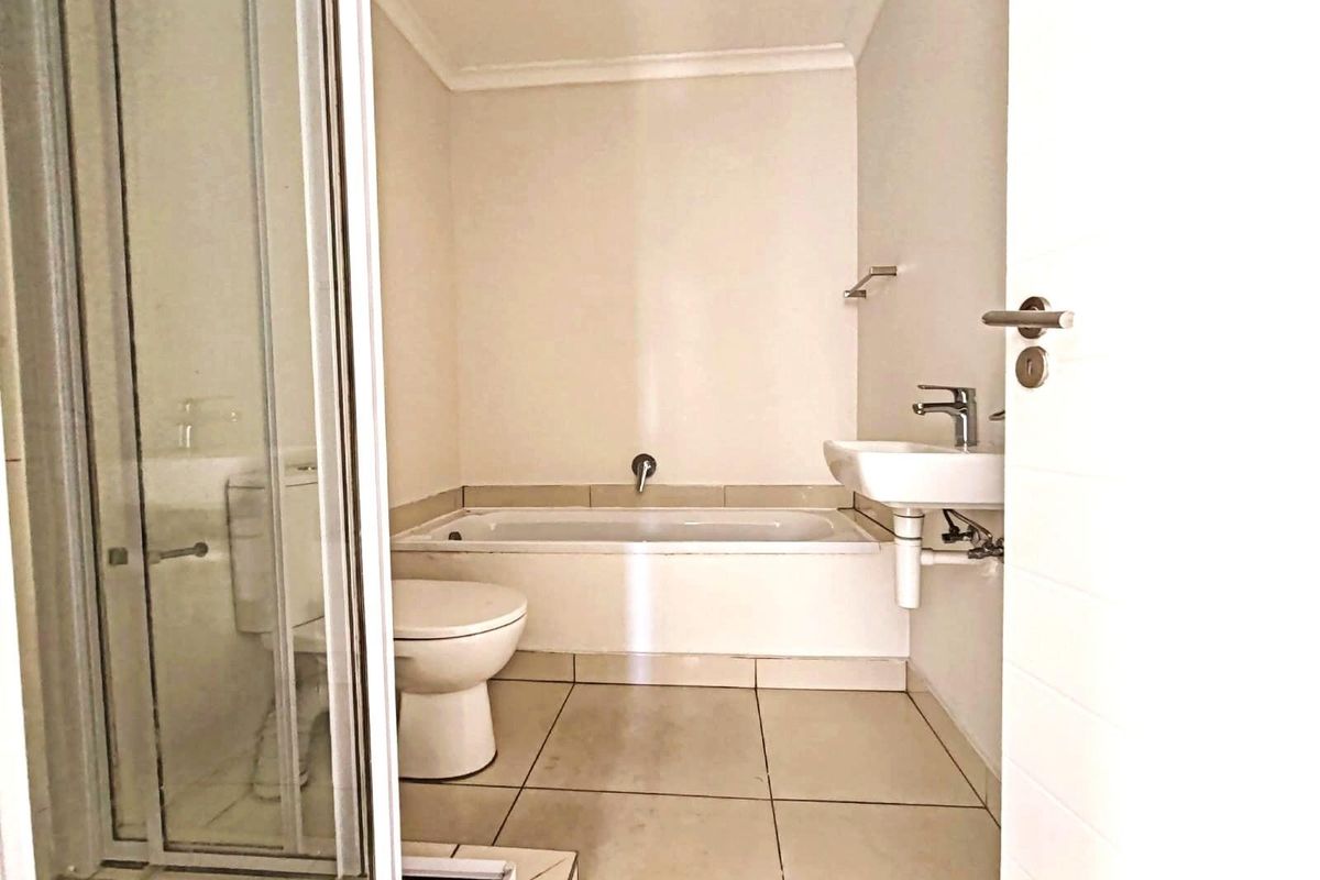 A functional bathroom featuring a built-in bathtub, a separate shower enclosure, a wall-mounted basin, and a toilet with tiled flooring.