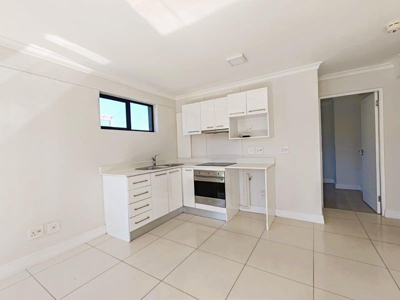 A clean, modern kitchen featuring white cabinetry, a built-in oven, hob, extractor fan, and tiled flooring in an open-plan layout.
