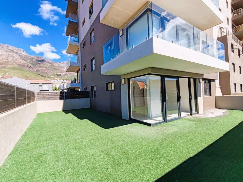 Ground floor apartment featuring a private artificial lawn garden, glass-enclosed patio area, and modern building facade with balcony access.