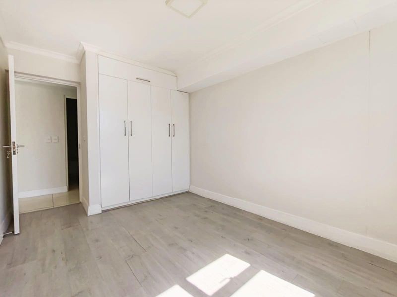 A bright, empty bedroom featuring light-toned laminate flooring and built-in floor-to-ceiling cupboards with modern hardware.