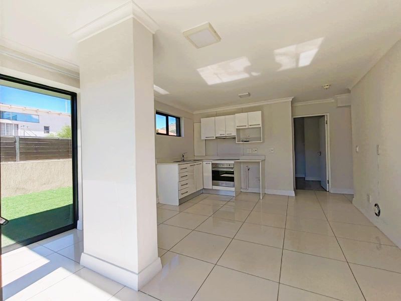 Open-plan kitchen and living area featuring tiled flooring, built-in cabinetry, integrated oven and hob, and direct access to an outdoor patio area.