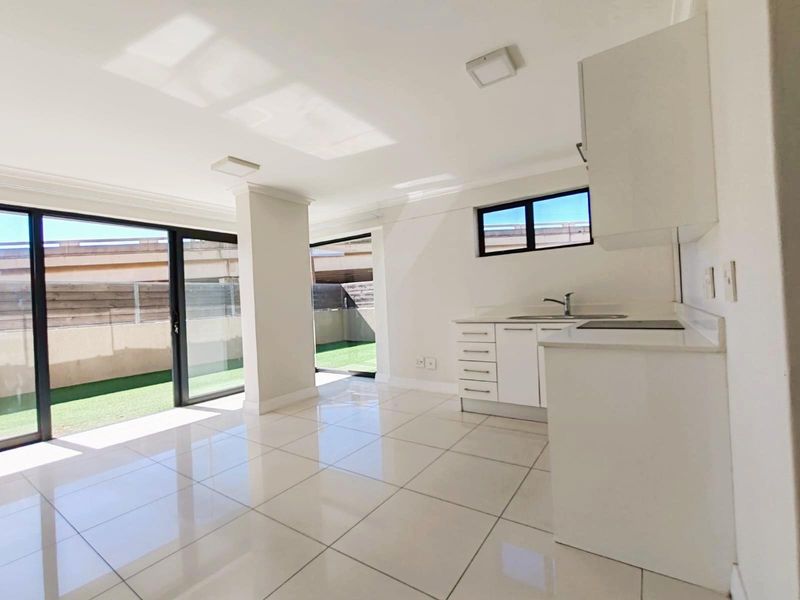 Bright open-plan living area featuring tiled flooring, a modern kitchen with built-in cabinetry, and large sliding glass doors leading to an outdoor space.
