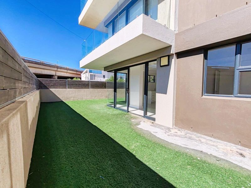 Private ground floor garden area with artificial turf, featuring a modern sliding door entrance and a balcony overhang from the upper level.