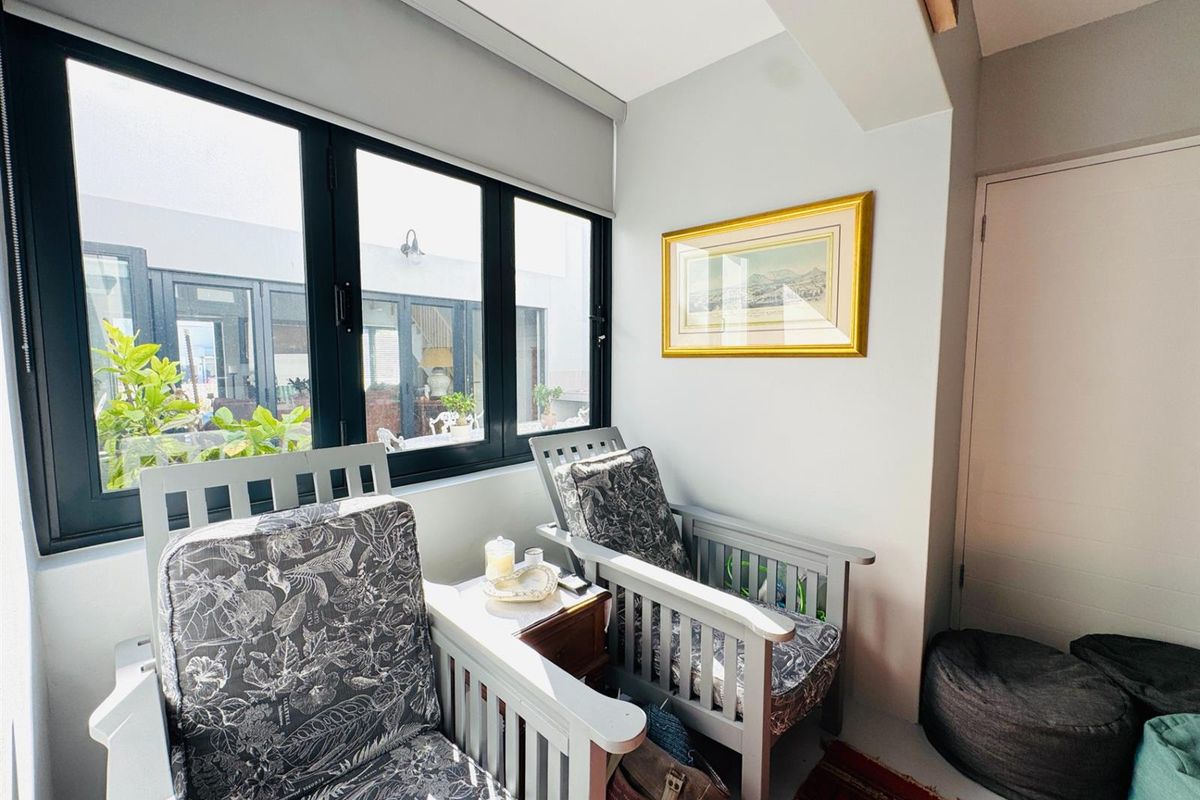 A bright sunroom or seating area featuring large black-framed windows that provide natural light and a view of the outdoor patio area.