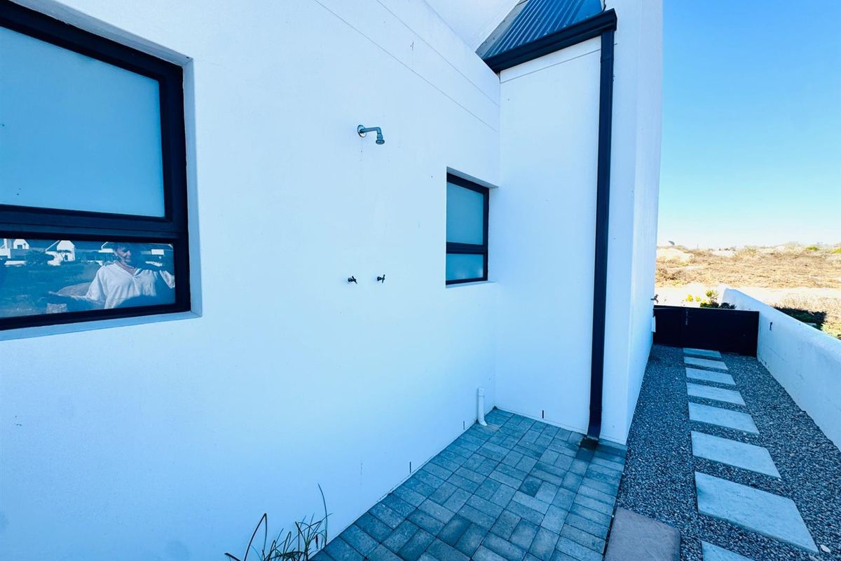 Exterior side passage featuring paved walkway, gravel landscaping, and a wall-mounted outdoor shower fixture.