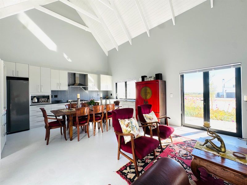 Spacious open-plan living and kitchen area featuring high vaulted ceilings, modern cabinetry, integrated appliances, and large glass doors leading to the exterior.