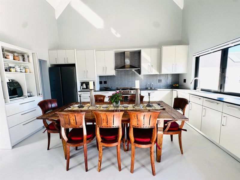 Spacious open-plan kitchen and dining area featuring high vaulted ceilings, modern cabinetry, a tiled backsplash, and a built-in stainless steel extractor fan.