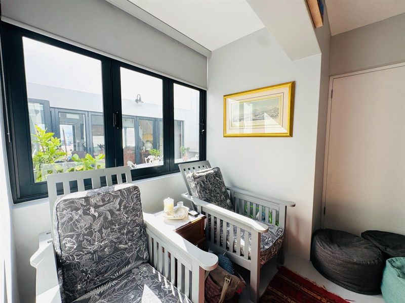 A bright sunroom or seating area featuring large black-framed windows that provide natural light and a view of the outdoor patio area.