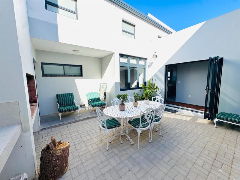 A paved outdoor patio area featuring a built-in brick braai, accessible via large folding doors from the interior living space.
