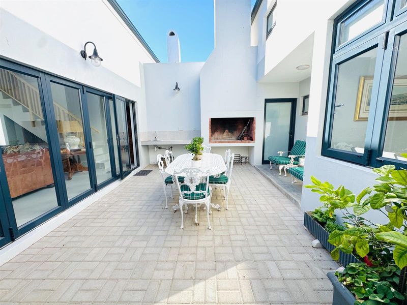 A private paved courtyard featuring a built-in braai, outdoor sink, and large glass sliding doors providing seamless indoor-outdoor flow.