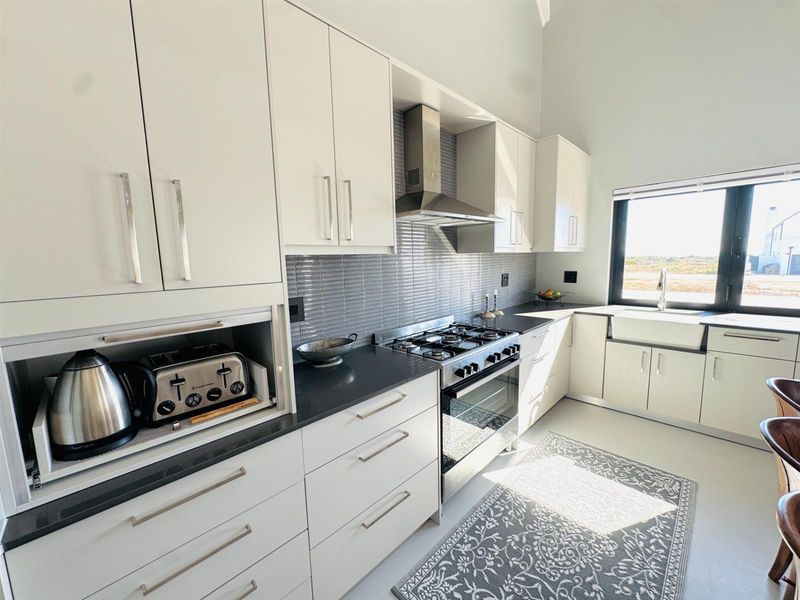 Modern kitchen featuring white cabinetry, dark stone countertops, a gas hob, stainless steel extractor fan, and a farmhouse-style sink with large window views.