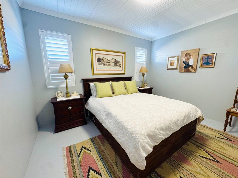 A well-maintained bedroom featuring white timber-paneled ceilings, plantation shutters, and neutral wall finishes.