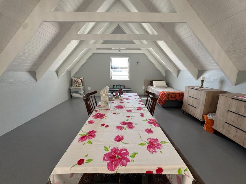 Spacious attic bedroom featuring exposed timber rafters, vaulted ceilings, and neutral flooring, offering a versatile living or hobby space.